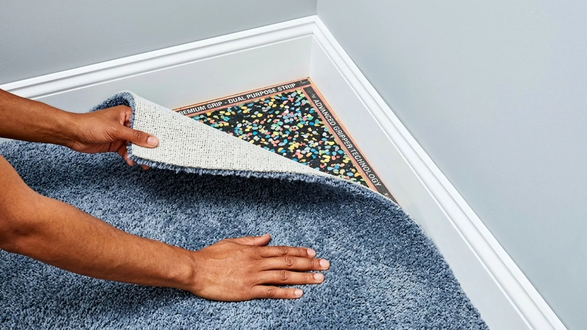 A close-up of a professional carpet underlay Geelong installation, showing hands pulling back plush blue carpet.