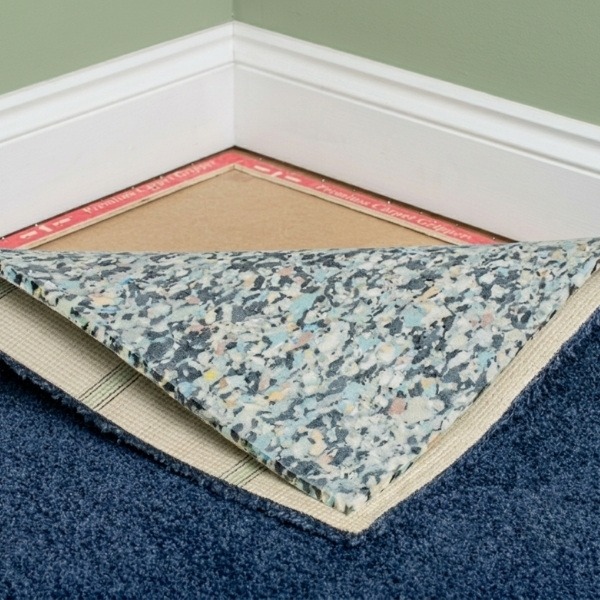 A room corner showing a carpet underlay installation in Canberra, featuring a layer of speckled foam padding beneath a plush blue carpet.